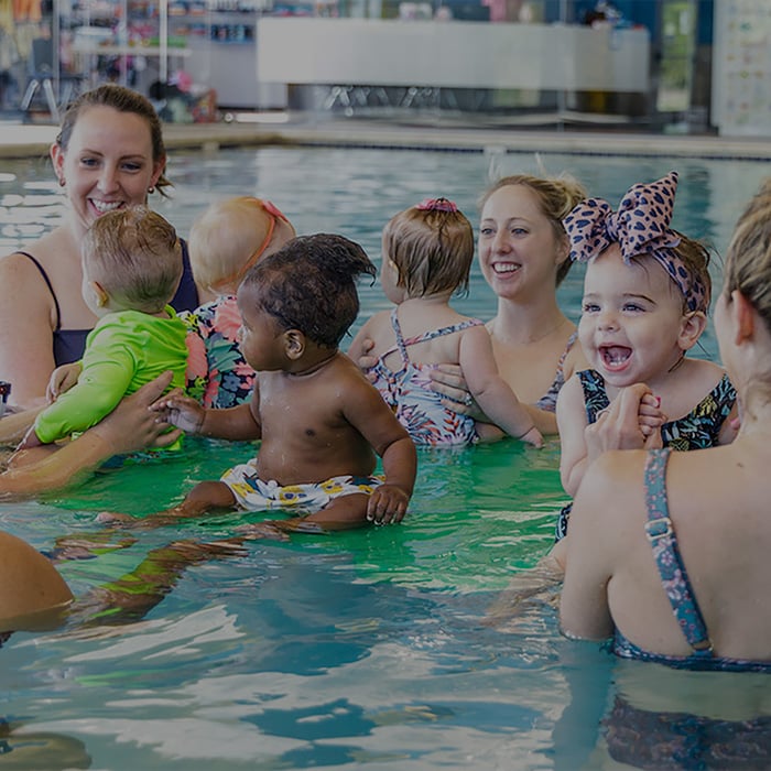 several-moms-helping-toddlers-balance-on-floatation-device-crop-overlay